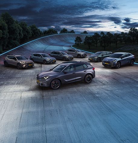 The 2024 Century bronze matte CUPRA Formentor parked on a reflective waterfront promenade. The sporty and aerodynamic new vehicle is positioned centre frame. The setting features futuristic architecture and Barcelona’s glowing city skyline at dusk.