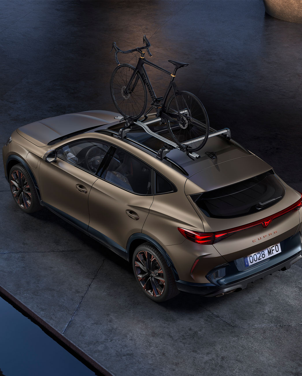 Vue aérienne du CUPRA Formentor 2024 century bronze matt avec porte-vélos, voiture garée sur le béton au crépuscule.