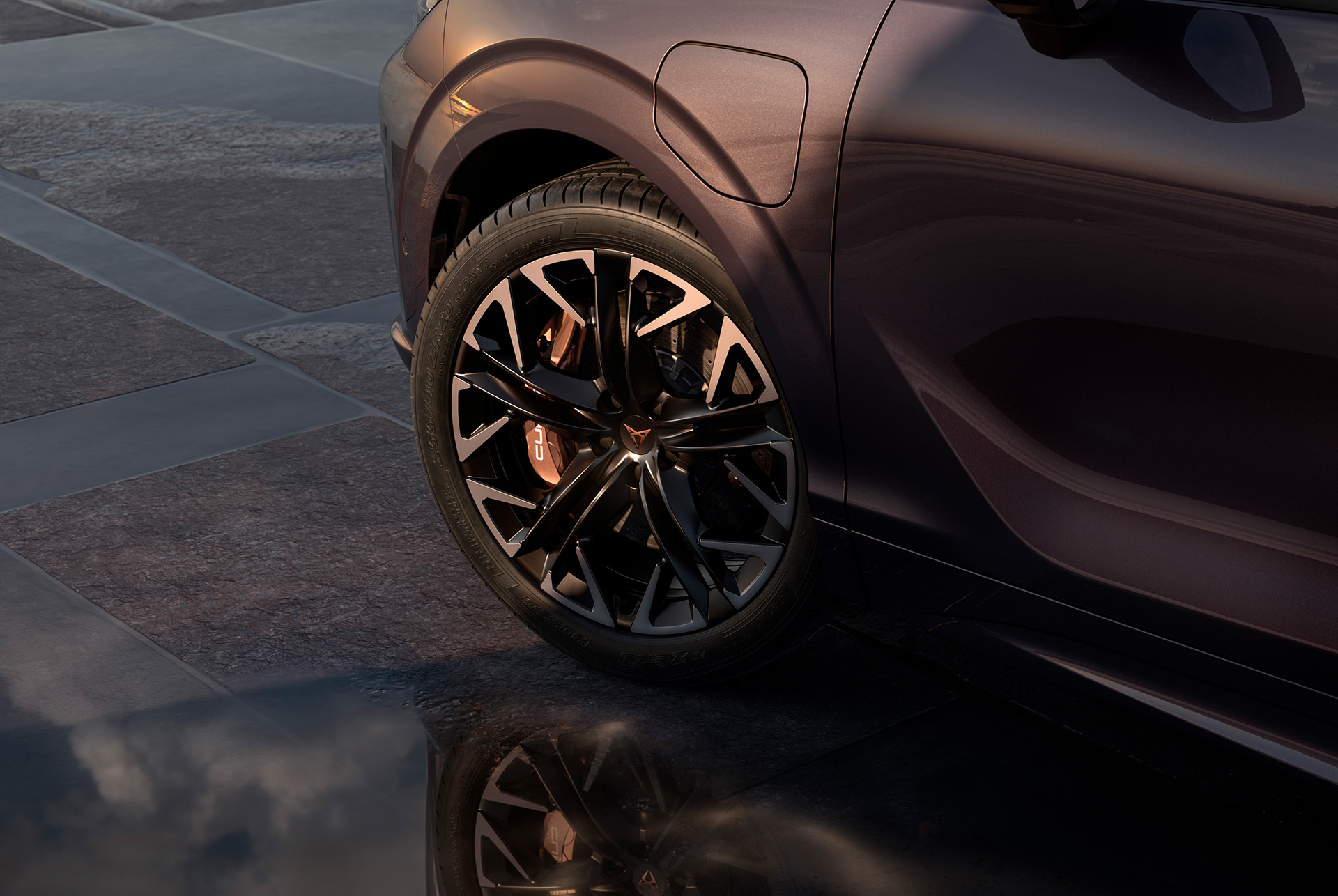 20 inch hadron alloy wheel on the new cupra terramar, in black with copper accents. Background includes a tiled pavement and part of the car's glossy, dark body.