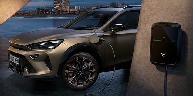 century bronze electric cupra formentor suv plugged into an EV charging wallbox with a city skyline in the background