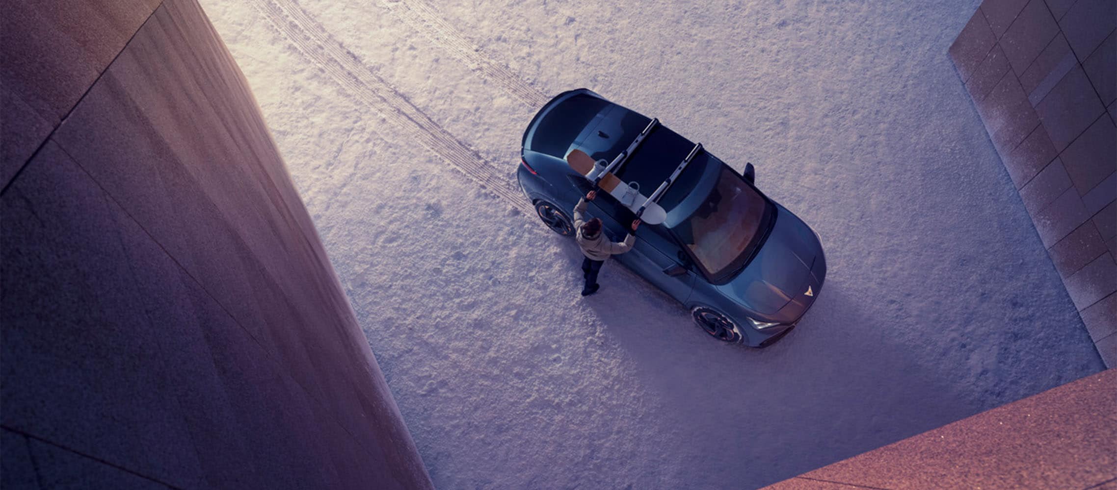 bev in the snow during winter months, cupra tavascan driver making adjustments to the roof rack in a snowy setting, birds eye view